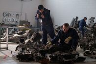 Mayday - Alarm im Cockpit – REENACTMENT - Inside an investigative hangar, the IAC on-site investigator (played by Drew Zeran) inspects what's left of the debris from the crash of Fly Dubai Flight 981, while the on-site assistant investigator documents their findings. (Cineflix 2021/Darren Goldstein)