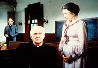 Unsere kleine Farm – Mrs. Oleson (Katherine MacGregor, l.) gesteht Reverend Alden (Dabbs Greer, M.), dass sie seinen Vorgesetzten, Dekan Dean Harmon (William Shallert, hinten), nach Walnut Grove gerufen hat, um eine Ehe mit Anna Craig zu verhindern.