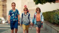 Geschichten vom Franz – Drei sommerlich gekleidete Kinder mit Sonnenbrillen und Rucksäcken laufen nebeneinander auf einem Fußweg.