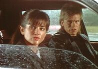 MacGyver – Mary Ruth (Penny Pyser, l.) und MacGyver (Richard Dean Anderson, r.) beobachten aus dem Auto zwei verdächtige Männer.