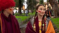 Home Sweet Rome – Lucy (Kensington Tallman, r.) und Nico (Christian Monaldi, l.) tragen Schals und Perücken in den Farben ihrer Fußballmannschaft - orange und rot.