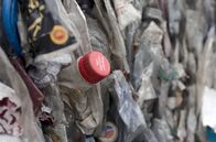 Coca-Cola und das Plastikproblem – Aufschrift „Bitte recyceln“ auf dem Verschluss einer Colaflasche inmitten von PET-Kunststoffballen, die in der Recyclinganlage von Viridor in Großbritannien sortiert werden