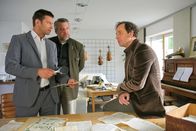 Die Rosenheim-Cops – Nach einem Gespräch mit dem Notenexperten Klaus Rieger (Stefan Drücke, r.) nimmt der aktuelle Fall von Hansen (Igor Jeftić, l.) und Stadler (Dieter Fischer, M.) eine überraschende Wendung.