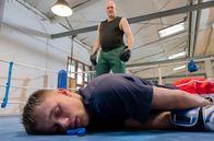 In aller Freundschaft – Finn Mohrbach (Tristán López, liegend) geht bei einer Einheit mit seinem Boxtrainer Ralf Brock (Rainer Haustein, oben) zu Boden.