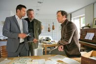 Die Rosenheim-Cops – Nach einem Gespräch mit dem Notenexperten Klaus Rieger (Stefan Drücke, r.) nimmt der aktuelle Fall von Hansen (Igor Jeftić, l.) und Stadler (Dieter Fischer, M.) eine überraschende Wendung.