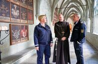 WaPo Bodensee – Paul Schott (Tim Wilde, r.) und Nele Fehrenbach (Floriane Daniel, l.) treffen Abt Barnabas (Ulrich Gebauer, M.) im Kreuzgang von Kloster Oberzell.