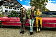 Falsche Siebziger – Gruppenphoto mit Geltinger Schwindler-Trio vor farbiger Strechlimousine: Gerhard Wittmann (Karl Kainz), Sebastian Bezzel (Hubertus Hochstetter), Kathrin von Steinburg (Iris Schranner)