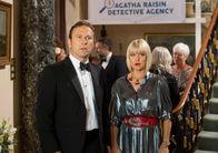 Agatha Raisin – Charles Fraiths (Jason Merells) und Agatha Raisin (Ashley Jensen) sind verwirrt, als sie James mit Melissa zusammen sehen, die sich Agatha anschließend als James‘ Schreibpartnerin vorstellt.