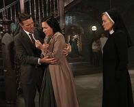 American Horror Story – Jahr 1964: Jude (Jessica Lange, r.) ist mittlerweile überzeugt, dass die echte Anne Frank (Franka Potente, M.) in Briarcliff Zuflucht gefunden hat. Plötzlich taucht jedoch der Ehemann (David Chisum, l.) der Patientin auf und behauptet, Anne sei in Wirklichkeit seine geliebte Frau Charlotte Reilly ...