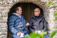 Mythos Ungesund – v.li.: Hanno Settele und Bernhard Hufnagl unterhalten sich in Eingangsbereich eines Steinhäuschen und suchen Schutz vor dem Regen.