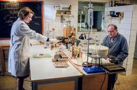 Charité – Hausmeister Fritz "Pflaster" (Uwe Preuss, r.) besucht Dr. Ella Wendt (Nina Gummich, l.) im Labor. Er hat sich bei der Arbeit am Finger verletzt.