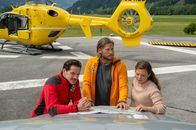 Die Bergretter – Tobias (Markus Brandl, l.), Markus (Sebastian Ströbel, M.) und Lara Fellner (Leonie Rainer, r.) besprechen am Heliport die weitere Vorgehensweise.