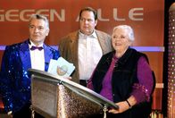 Der Bulle von Tölz – Der Mörder kündigt an, Claasen (Henry Hübchen, l.) während seiner Show zur Strecke zu bringen. Wird es Benno (Ottfried Fischer, M.) und Resi (Ruth Drexel, r.) gelingen, einen Mord vor laufenden Kameras zu verhindern?
