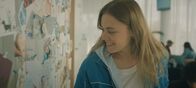 The Club – Charlie (Roos Dickmann) amüsiert sich im Wartebereich der Kinderwunschklinik über die ungewöhnlichen Namen einiger Kinder, die auf Geburtskarten zu lesen sind.