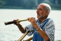 Löwenzahn Classics – Peter Lustig sitzt in einem Boot auf dem Bärstädter See und beobachtet die Natur durch sein Fernglas.