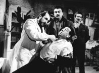 Don Camillos Rückkehr – Mit Genuss beobachtet Peppone (Gino Cervi, Mitte), wie sich sein Lieblingsfeind Don Camillo (Fernandel, sitzend) versucht, sich dem Zahnarzt zu widersetzen.