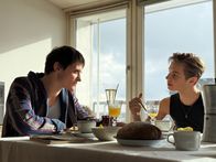 AIDS - In Zeiten der Liebe – Heiko (Evangelos Tsarkowistas, l.) doziert begeistert über das Theater und seine Vorstellung von Bühne - auch beim Frühstück. Nikolaus (Konrad Damer, r.) hört ihm zu.