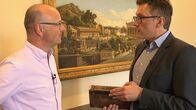 SMS - Schwanke meets Science – Karsten Schwanke (links) im Gespräch mit dem Generalsekretär des Deutschen Archäologischen Instituts (DAI), Philipp von Rummel, in Berlin. Rummel hält die Erstausgabe der archäologischen Nachrichten aus dem Gründungsjahr des Instituts 1829 in Händen.
