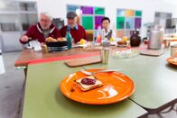 Digiclash: Der Generationen-Contest – Ralf, Jürgen und Renate vom Team Digital sitzen beim ersten gemeinsamen Frühstück an einem üppig gedeckten Frühstückstisch. Das Frühstück von Team "Real" fällt hingegen etwas spartanischer aus.