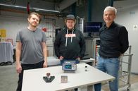 Einfach genial – Das Erfinder-Duo Dimitri Benke (links) und Dr. Maximilian Fries aus Darmstadt sowie Prof. Oliver Gutfleisch (rechts). Auf dem Tisch liegt im Vordergrund die Erfindung, das magnetische Kühlsystem, dahinter ein Messgerät. Porf. Gutfleisch wird Erfindung testen.