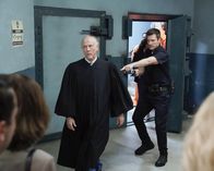 The Rookie – Der Richter Stevens (Jim Ortlieb, l.) wollte John Nolan (Nathan Fillion, r.) und weitere Besucher des Gerichts aus Platzgründen nicht in den Bunker lassen und hatte sie sogar mit einer Waffe bedroht, die ihm John abgenommen hat.