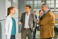 Die Rosenheim-Cops – Pathologin Mai (Sina Wilke, l.) teilt Hansen (Igor Jeftic, M.) und Stadler (Dieter Fischer, r.) ihre neuen Erkenntnisse mit (im Hintergrund: Komparsen).