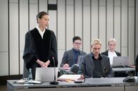 Conti: Meine zwei Gesichter – Staatsanwältin Henry Mahn (Malaya Stern Takeda, li.) verliest die Anklageschrift. Nebenkläger Matt Westphal (Daniel Sträßer, 2.v.r.), Ex-Partner der Angeklagten und Vater des toten Kindes, versucht den Blicken der gegnerischen Seite auszuweichen.