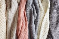 Ovanti Strickdesign – Bunch of knitted warm pastel color sweaters with different vertical knitting patterns hanging in bunch, clearly visible texture. Stylish fall / winter season knitwear clothing