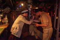 ZDF-History: Das Boot - Die Dokumentation – Ein U-Boot-Kommandant blickt durch das Sehrohr eines U-Bootes und sichtet ein Schiff. Neben dem Sehrohr stehen zwei Offiziere.