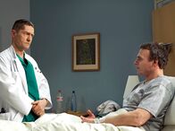 In aller Freundschaft – Reinhold Wollenberg (Oliver Breite, rechts) lässt sich von Dr. Kaminski (Udo Schenk) wegen einer Entzündung behandeln. Andrea Wollenberg, Reinholds Frau, ist eine Kollegin von Dr. Kaminski. Als Kaminski nachfragt, warum Reinhold sich nicht von seiner Frau behandeln lässt, weicht er aus.