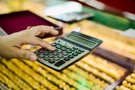 Deal Makers - Alles hat seinen Preis – Finger press the calculator to calculate the purchase of gold jewelry with blurry gold jewelry in showcase at the gold shop.