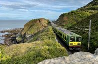 alpha-expedition: Mit dem Zug ... – Der DART lässt die letzte Klippe hinter sich liegen: Der Nahverkehrszug zwischen Greystones und Bray fährt auf eingleisiger Strecke. Parallel zur Bahn verläuft ein Spazierweg, der Cliff Walk.
