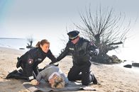 Notruf Hafenkante – Franzi (Rhea Harder, l.) und Henning (Uwe Fellensiek, r.) finden eine Frau (Saskia Vester, M.), die blutüberströmt am Elbufer zusammengebrochen ist.