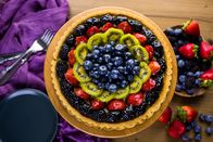 Das große Promibacken – Fresh fruit tart on cake stand on wood table.