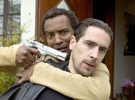 Mankells Wallander – Der verzweifelte Diao (Khalid Geire) nimmt Kommissar Stefan Lindman (Ola Rapace) als Geisel.
