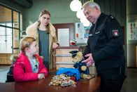Notruf Hafenkante – Wolle (Harald Maack, r.) ist froh, dass er der kleinen Lena (Malina Schächterle, l.), mit Hilfe seines Polizeibären, das von ihr sichergestellte Diebesgut entlocken konnte. Lenas Mutter Betti (Charlotte Puder, M.) versucht, noch einen Finderlohn für ihre Tochter rauszuschlagen.