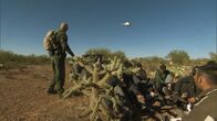 Amerikas heiße Grenze – Nogales, AZ: An agent signaling to a helicopter in the air, while a group of apprehended men sit on the ground. Helicopters have been beneficial in conducting high speed chases.