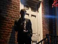 Love Kills – Bobby Lamont (Fletcher) at the top of the stairs in front of a white door looking at his phone.