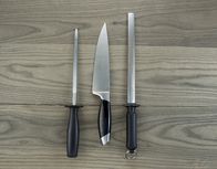 We love Cooking – Foto eines einzelnen großen Küchenmessers und zweier Schärfgeräte auf gealtertem Weißeschenholz