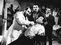 Don Camillos Rückkehr – Mit Genuss beobachtet Peppone (Gino Cervi, Mitte), wie sein Lieblingsfeind Don Camillo (Fernandel, sitzend) versucht, sich dem Zahnarzt zu widersetzen.