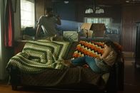 Tödliche Stille – A woman laying down on a couch while a man drinks a beer in the background.