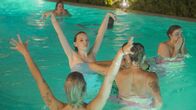 Wild Wild Wedding – The Wedding Guests are in the pool, two blond girls are stretching their arms to the sky.