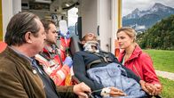 Watzmann ermittelt – Jerry Paulsen (Peter Marton, liegend) hatte einen Unfall: An seinem Dienstwagen haben die Bremsen versagt. Johanna (Ines Lutz, r.) und ihr Vater Benedikt Beissl (Andreas Geibel, l.) sind zur Stelle, wie der verletzte Jerry in den Krankenwagen geladen wird. Sanitäter (Komparse, 2.v.l.)