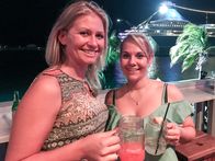 Verrückt nach Meer – Die Freundinnen Jana und Eileen in der Bar Lukka Kairi am Hafen von Nassau / Bahamas mit der Grand Lady im Hintergrund. Auch die Passagierinnen Jana und Eileen wollen heute noch etwas erleben. Da das Schiff erst am späten Abend ablegt, gehen sie noch auf einen Drink an Land.