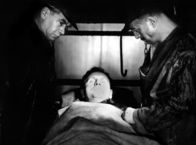 Sonnensucher – In einem Schacht der Wismut AG ist ein Brand ausgebrochen. Obwohl die Kumpel, unter ihnen Jupp König (Erwin Geschonneck, r.) und Oberst Fedossjew (Wladimir Jemeljanow), alles für die Rettung der Eingeschlossenen tun, erliegt der Vorarbeiter Beier (Günther Simon) seinen Verletzungen.