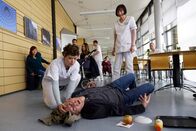 In aller Freundschaft – Claus Wieding (Johannes Hitzblech, liegend) wollte nur schnell etwas ind er Cafeteria besorgen, als er einen epileptischen Anfall bekommt. Schwester Svenja Werth (Laura Louisa Garde, li.) ist sofort bei ihm und weiß genau, was zu tun ist. Bei den anderen Gästen (Komparsen) sitzt der Schreck tief.