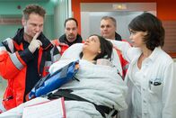 Notruf Hafenkante – Dr. Haase (Fabian Harloff, l.) hat Schwester Adriana (Christina Geiße, liegend) versprochen, weder Dr. Jonas (Gerit Kling, r.) noch sonst jemandem ihr Geheimnis zu verraten. Zwei weitere Sanitäter (Komparsen) helfen beim Transport.