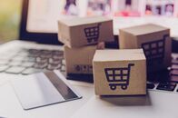 Dauerwerbesendung – Online-Shopping - Papierkartons oder Pakete mit einem Einkaufswagen-Logo und einer Kreditkarte auf einer Laptop-Tastatur. Shopping-Service auf der Online-Web und bietet Hauslieferung.